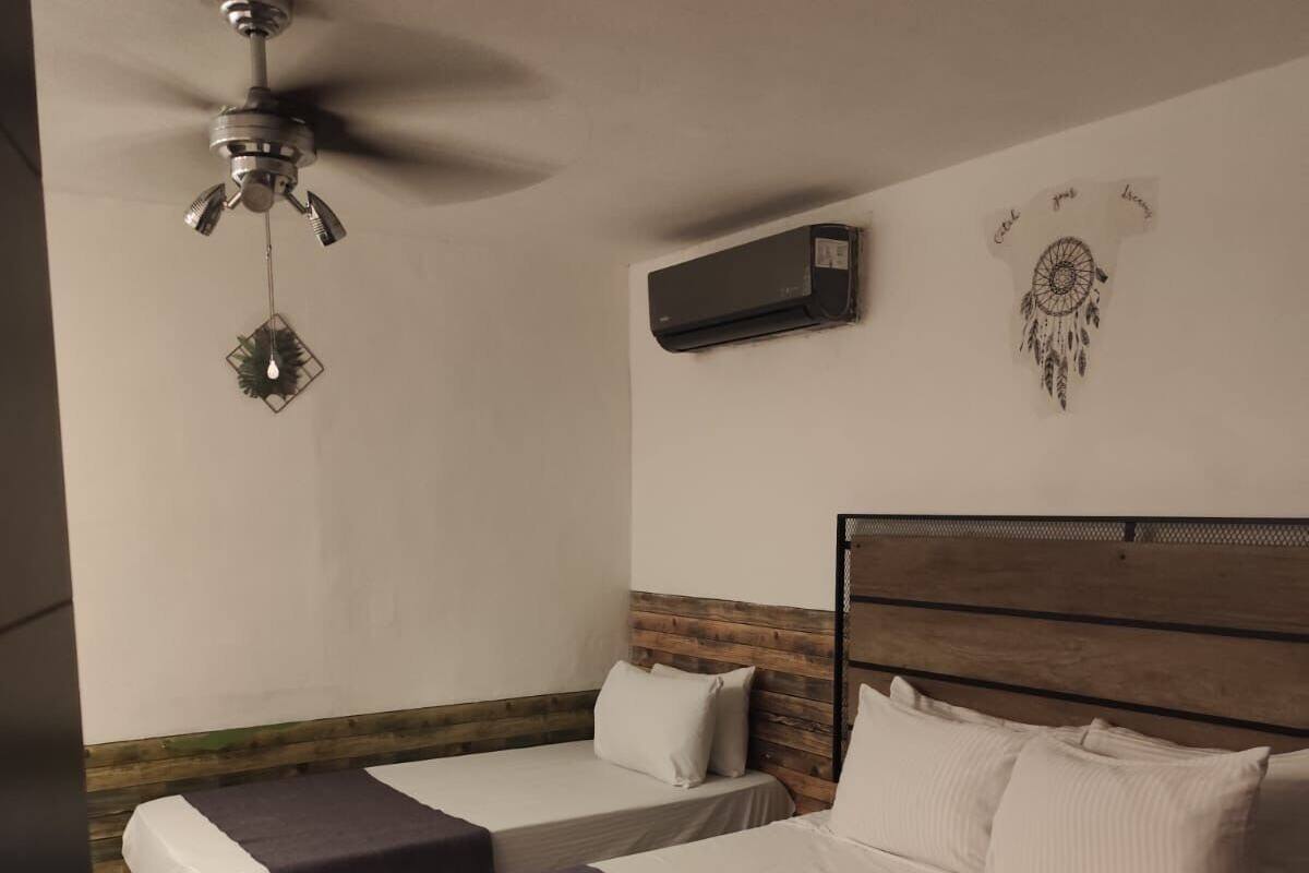 Habitación de hotel con dos camas, ventilador de techo, unidad de aire acondicionado y decoración con atrapasueños.