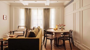 A well-lit living room with a sofa, a dining table with chairs, and a large window with curtains. - SLO Claridge House: 2BR apartment Mayfair (London)