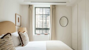Ein Hotelzimmer mit einem großen Bett, einem Fenster mit Vorhängen, einem gerahmten Bild an der Wand und einem runden Spiegel.