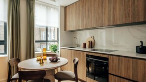 Eine moderne Küche mit Holzschränken, einer Marmorarbeitsplatte und einem eingebauten Backofen. Es gibt einen Essbereich mit einem runden Tisch und Stühlen, sowie ein Fenster mit Vorhängen.