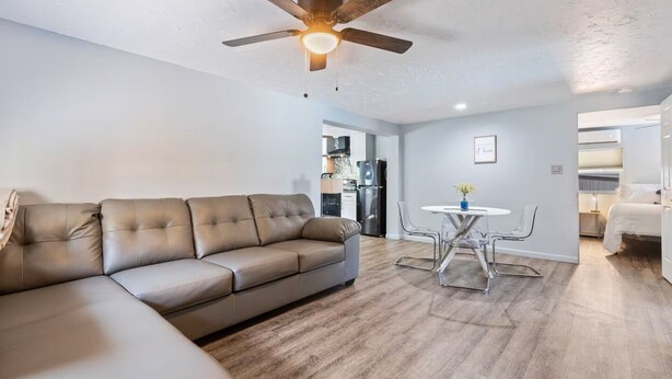 Un salon moderne avec un canapé en cuir, une table à manger avec des chaises, un ventilateur de plafond et, au fond, un coin cuisine.