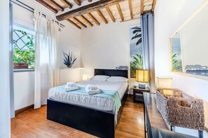 Een hotelkamer met een bed, nachtlampjes, een raam met gordijnen, een plant en een spiegel.