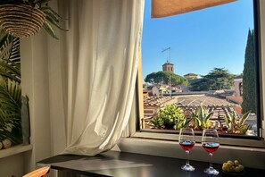 A window with a view of a cityscape, two glasses of red wine, and a potted plant on a windowsill. - Scala Top Apartment in Trastevere (Roma)