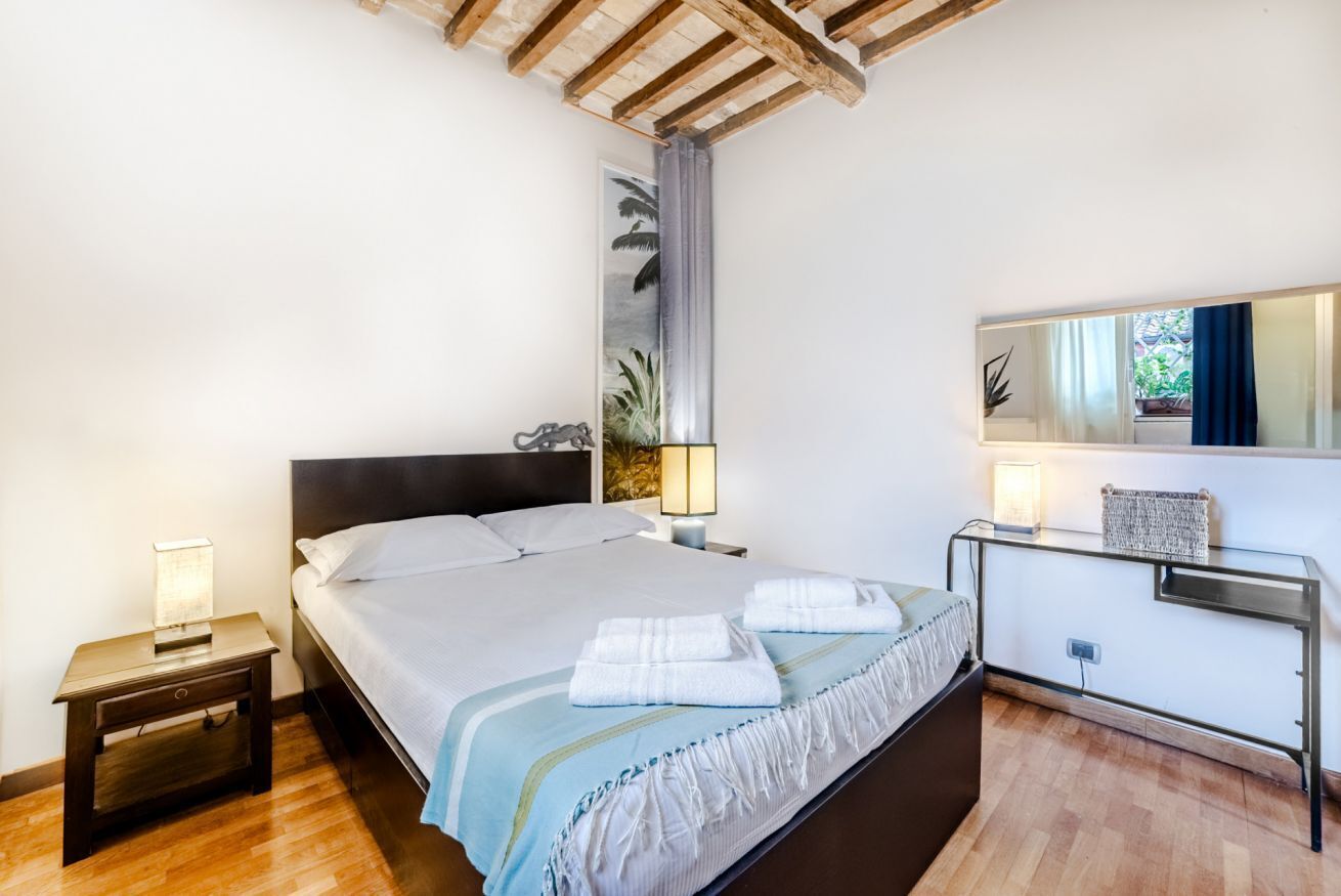 Une chambre à coucher avec un lit, des tables de chevet, une commode, un miroir et une fenêtre avec des rideaux.