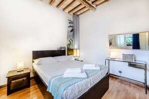 Un dormitorio con cama, mesitas de noche, un tocador, un espejo y una ventana con cortinas.