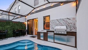 A modern outdoor kitchen with a built-in grill, a pool, and a seating area with chairs. - Modern 5BR Villa w/ Pool – 15 min to Disney (Orlando)