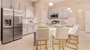 A modern kitchen with stainless steel appliances, white cabinetry, and a central island with bar stools. - Modern 5BR Villa w/ Pool – 15 min to Disney (Orlando)