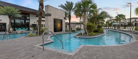 A modern pool area with a stone building, palm trees, and lounge chairs.