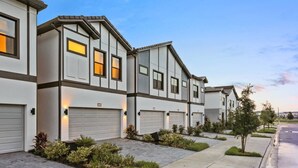 A row of modern townhouses with attached garages, neatly landscaped gardens, and a clear sky. - Modern 5BR Villa w/ Pool – 15 min to Disney (Orlando)