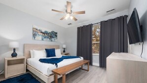 Una camera da letto con un letto, comodini, una ventola a soffitto, una finestra con tende e una televisione.