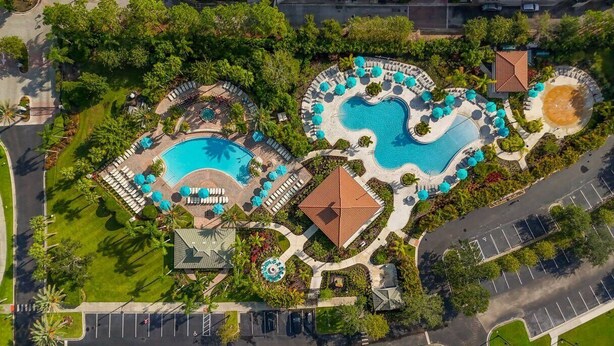 Una vista aerea di un resort con diverse piscine, lettini prendisole e un’area parcheggio.