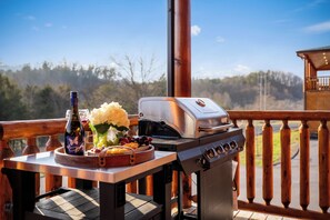 En grill på en træterrasse med et smukt udsyn til træer og en klar himmel.