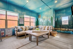 Una habitación con pared azul, una mesa de centro de madera, un sofá y una ventana que da a una valla de madera.