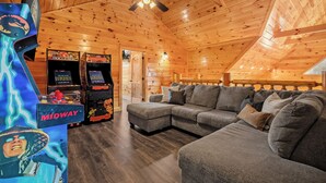Ein gemütliches Blockhaus-Interieur mit einer Eckcouch, Spielautomaten und einem Deckenventilator.