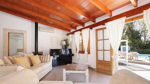 Amplia sala de estar con sofá, una mesa de centro y televisor. Se ve una piscina a través de las ventanas.