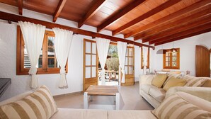 Amplia sala de estar con vigas de madera, ventanas grandes con cortinas y vistas al exterior.