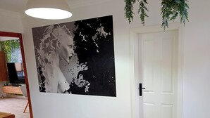 Um quarto com uma grande pintura abstrata na parede, uma porta branca e uma planta pendurada.