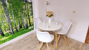 Uma sala de jantar com uma mesa redonda, quatro cadeiras brancas, um vaso com flores e um mural na parede retratando uma floresta.