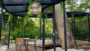 A wooden deck with a pergola structure, a table and chairs, and a hanging sign that reads "Congo Place".