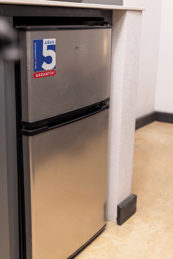 A compact, stainless steel refrigerator with a blue and red sticker indicating a 5-year warranty.