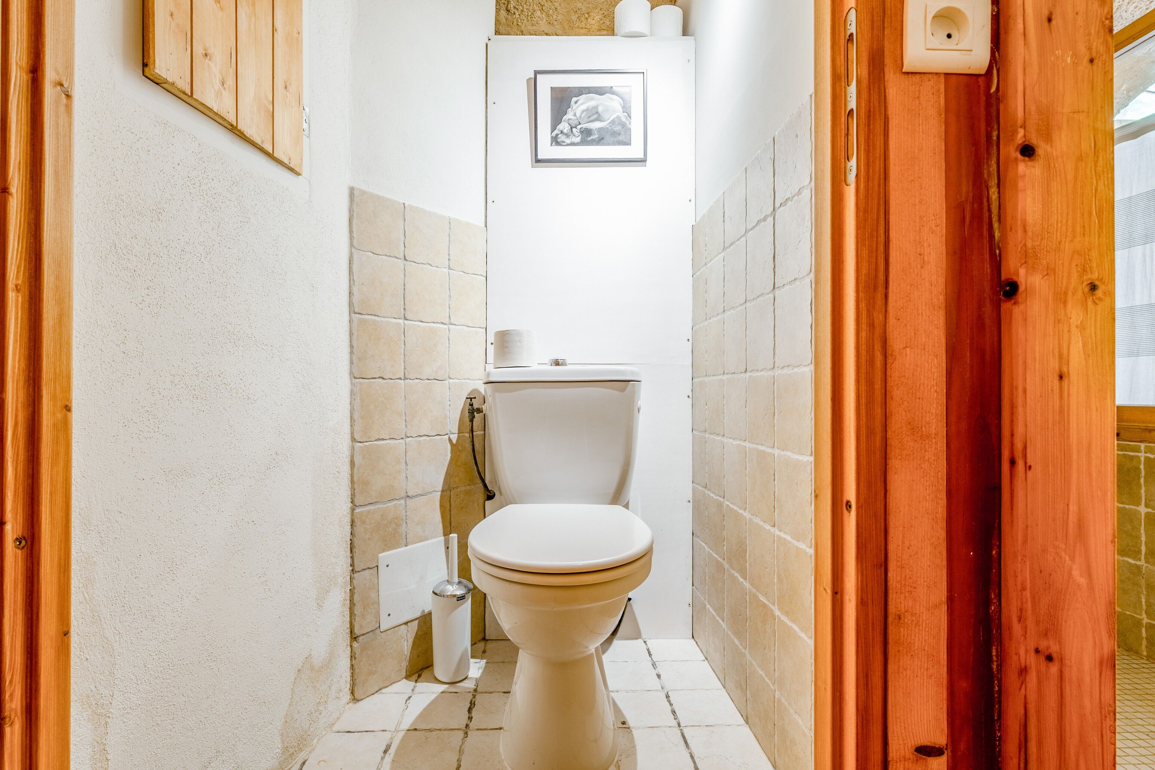Un baño pequeño con inodoro, un cuadro en la pared y una puerta de madera.