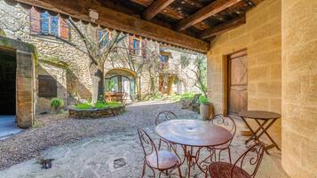 A stone building with a courtyard, a wooden ceiling, and a round metal table with chairs.