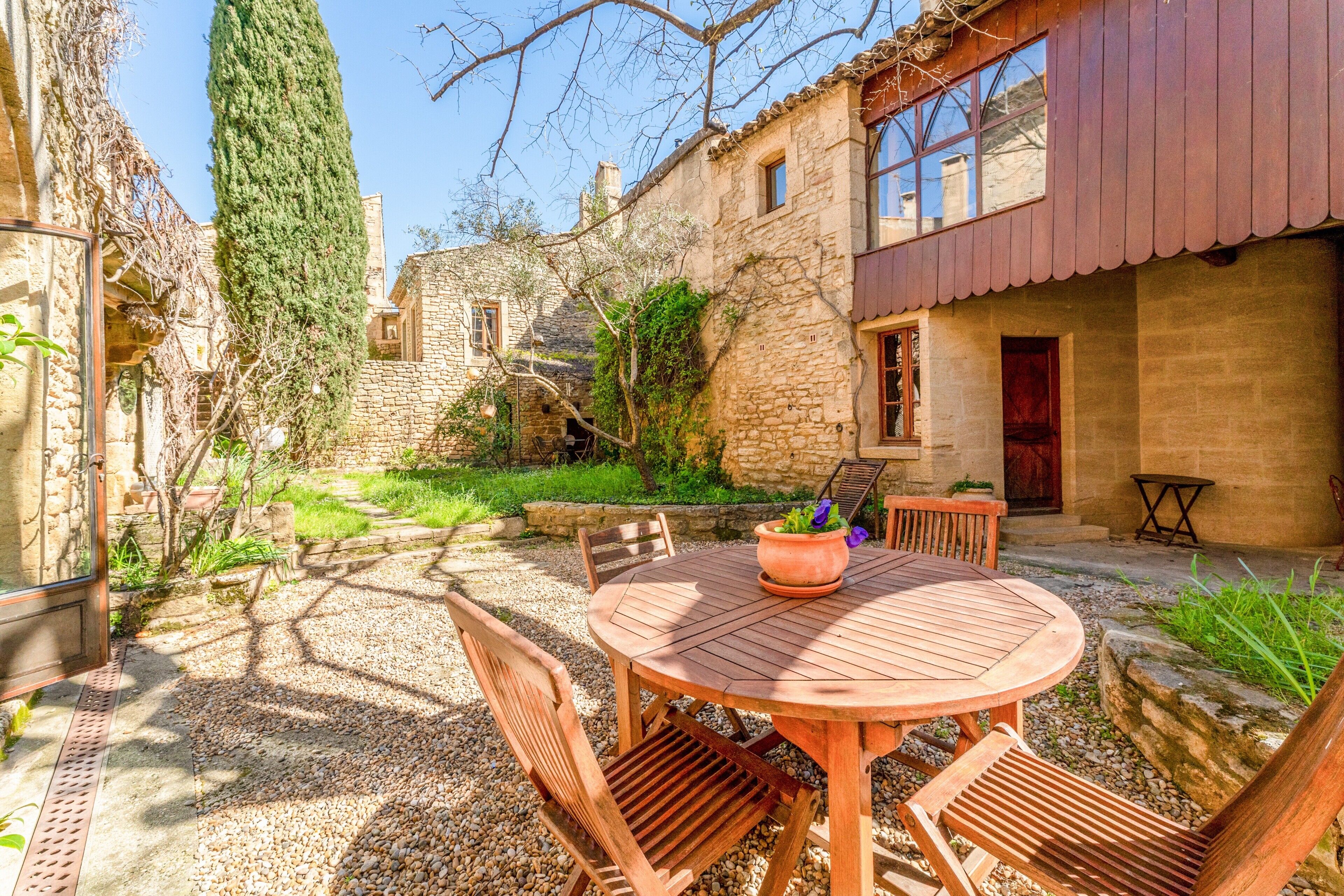 A stone building with a wooden table and chairs, a potted plant, and a gravel path.