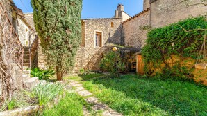 A stone building with a wooden door, a stone staircase, and a garden with grass and plants. - Guest Room “Room 1” with Shared Pool, Communal Terrace, and Wi-Fi (Vers Pont du Gard)