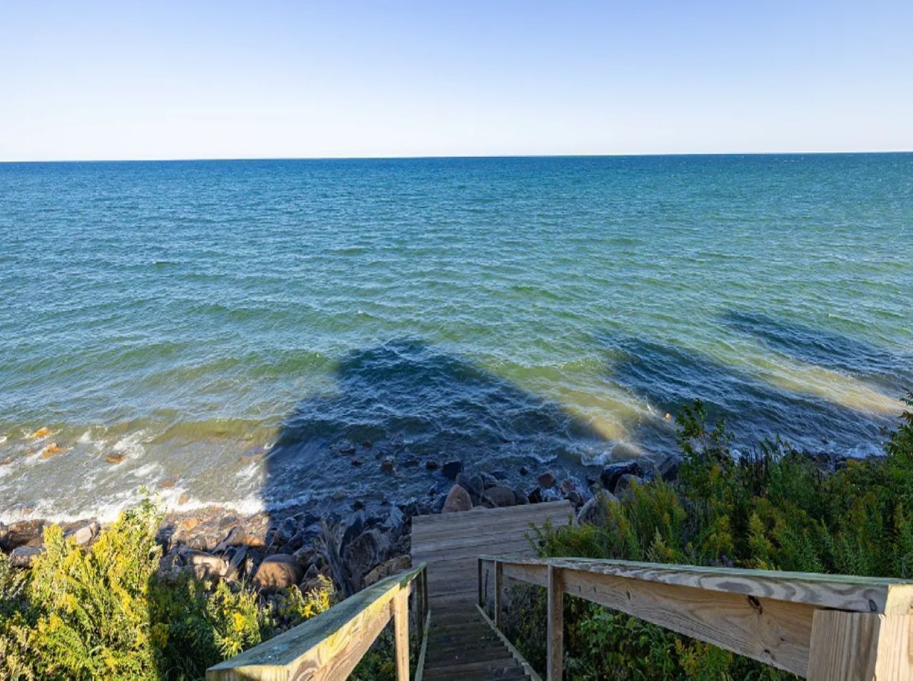 Ein hölzerner Steg führt zu einer felsigen Küste mit klarem, blauem Wasser.