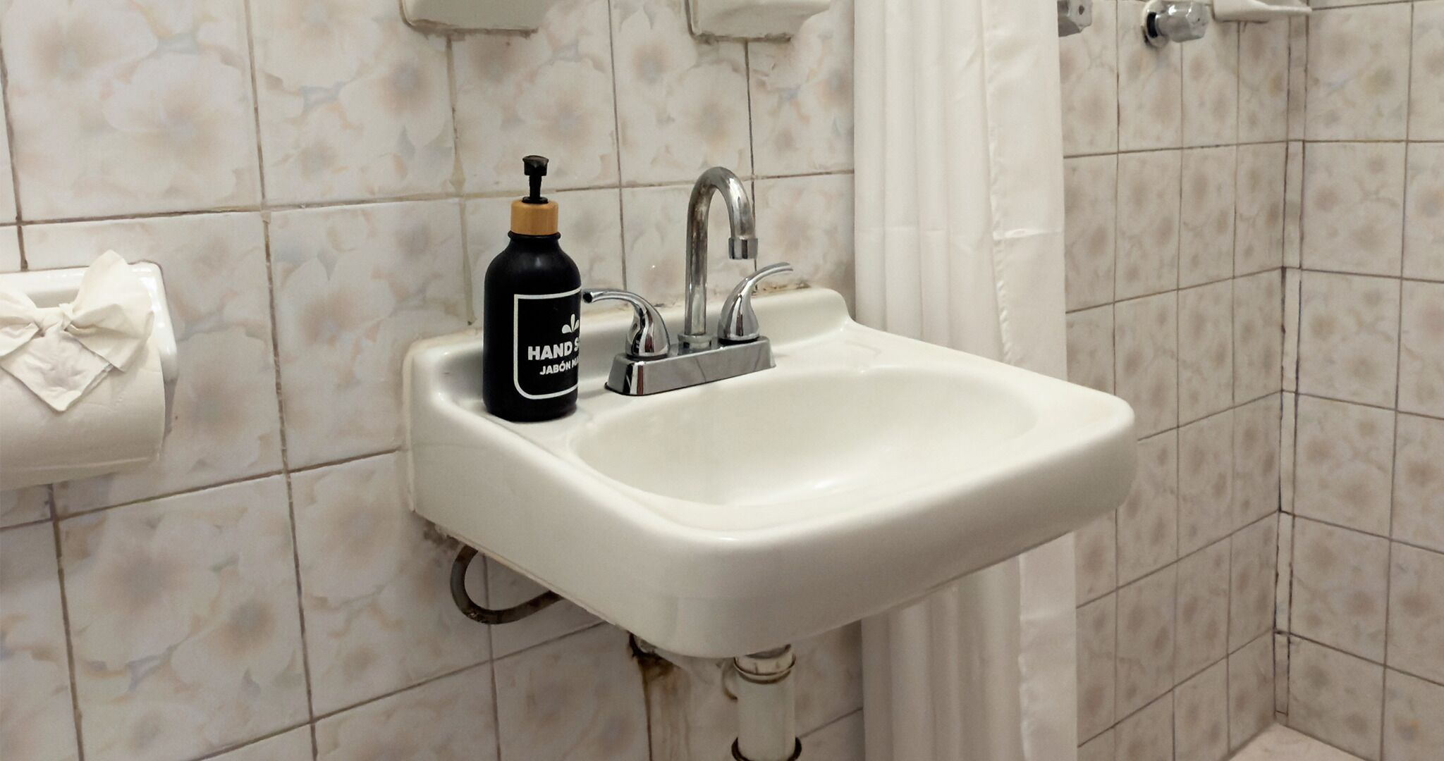 A bathroom sink with a hand soap dispenser, a towel dispenser, and a shower curtain.
