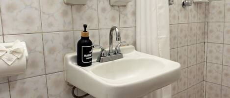 A bathroom sink with a hand soap dispenser, a towel dispenser, and a shower curtain.