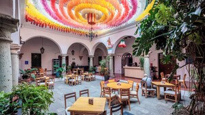 A spacious courtyard with multiple wooden tables and chairs, surrounded by arches and potted plants. - Hotel Posada Casa de la Tía (Oaxaca)