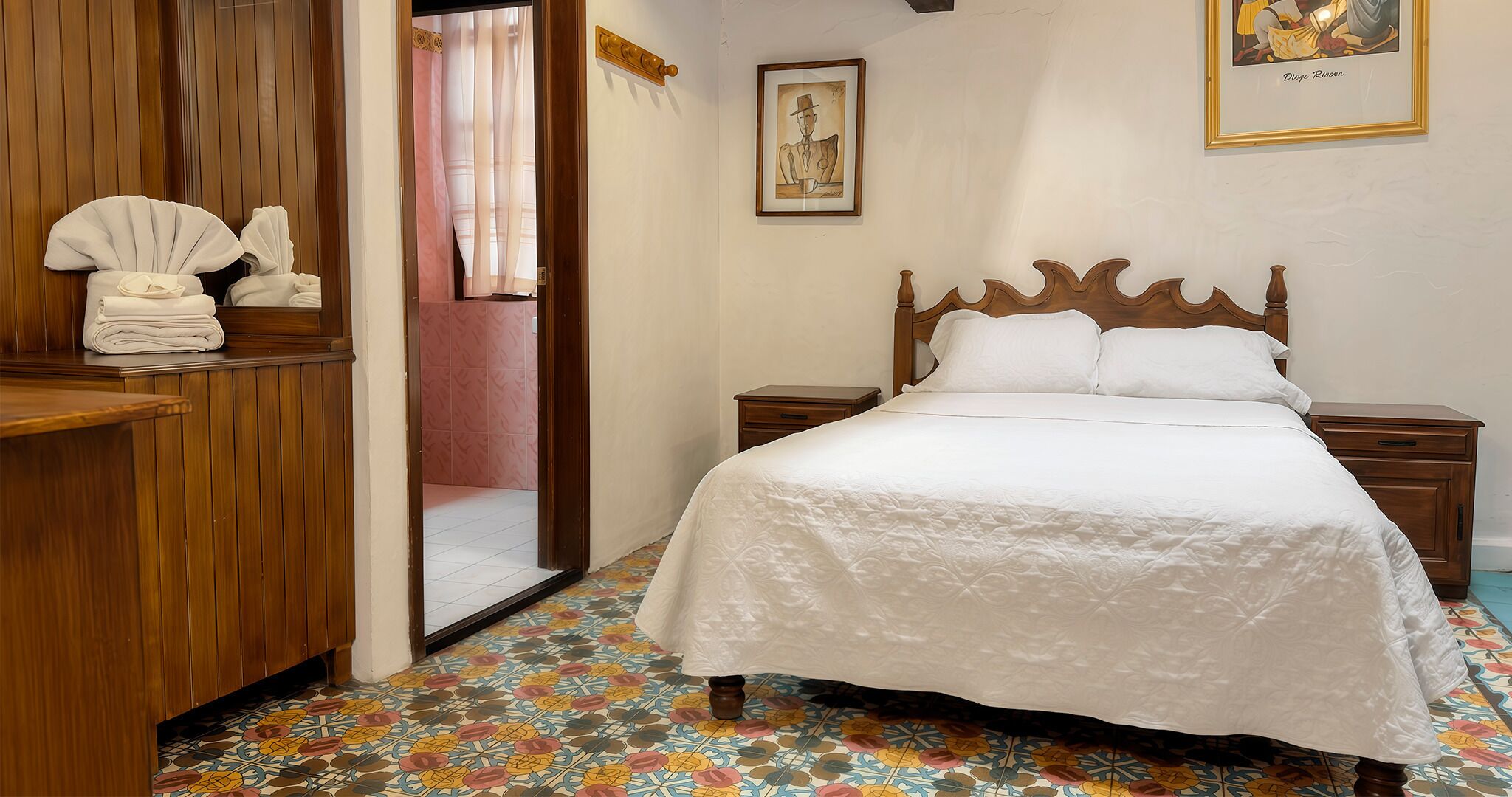 A bedroom with a wooden headboard, a bed with white bedding, a nightstand, a dresser, and a mirror.