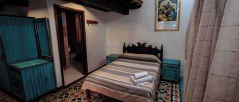 Un dormitorio con cama, una mesita, una silla, una puerta y un baño.