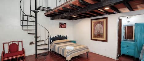 A bedroom with a spiral staircase, a bed, a red chair, and a blue wardrobe.