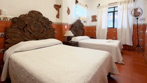 A hotel room with two beds, a wooden headboard, a nightstand with a lamp, a mirror, and a view of the outside through a window with curtains. - Hotel Posada Casa de la Tía (Oaxaca)
