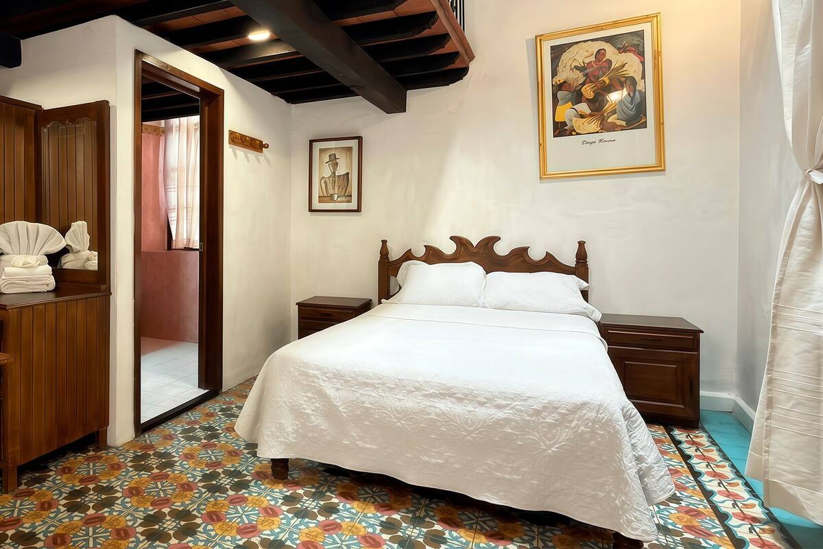 Quarto com cama, guarda-roupa de madeira e chão coberto por ladrilhos coloridos.