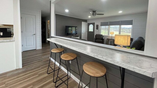 Una cocina moderna con encimera de mármol, dos taburetes de bar, un ventilador de techo y un televisor.