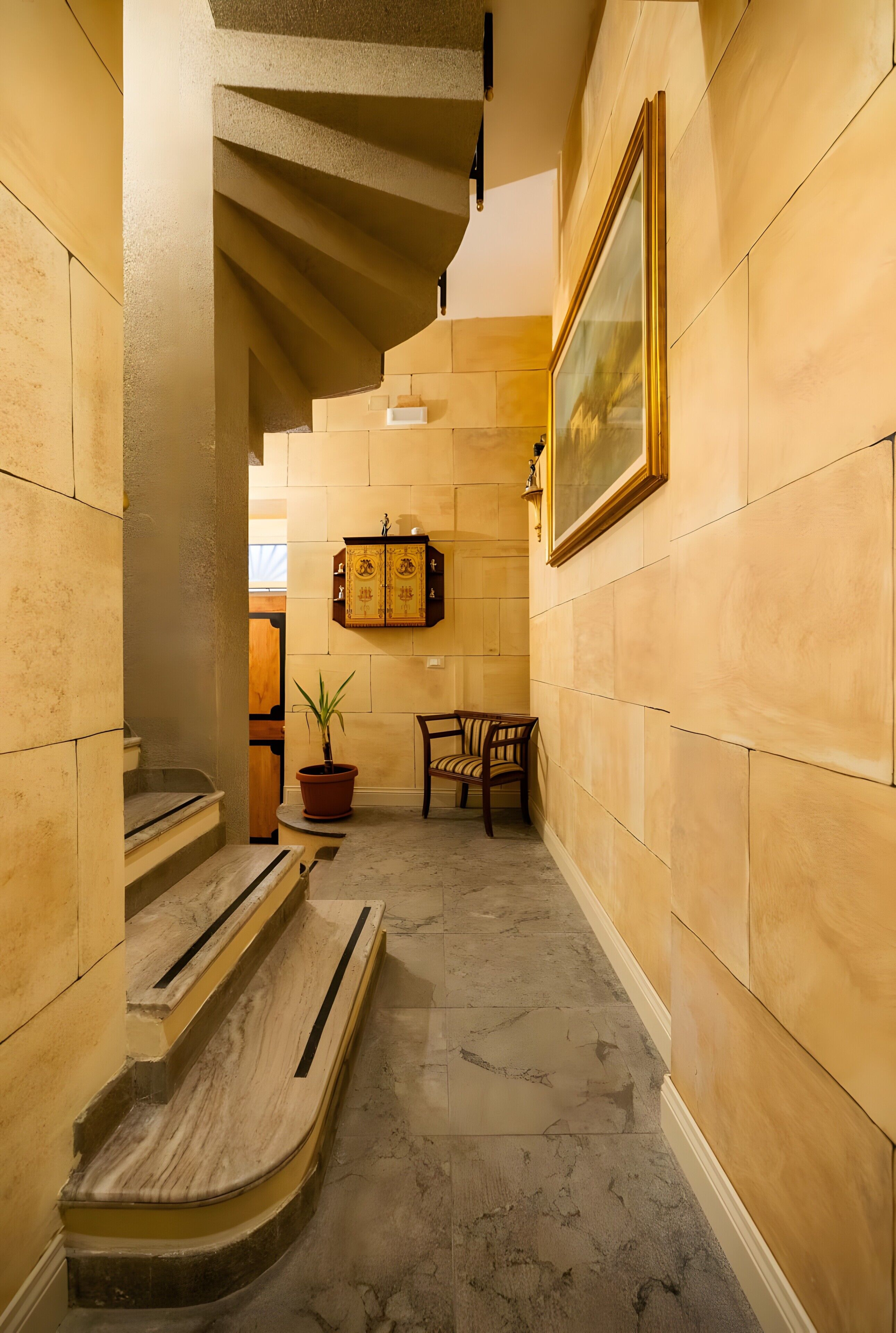 En hall med marmortrappsteg, en trästol, en krukväxt och en inramad tavla på väggen.
