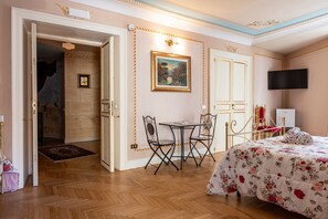 A hotel room with a bed, a desk with chairs, a painting on the wall, and a television. - Room 'Aurora' at Francy House Termini Imerese (Termini Imerese)