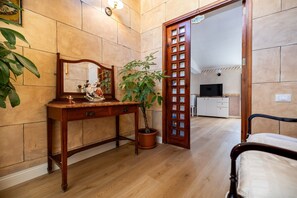 A room with a wooden dresser, a mirror, a potted plant, a bed, and a doorway leading to a kitchen. - Room 'Aurora' at Francy House Termini Imerese (Termini Imerese)