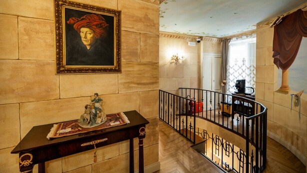 A hallway with a marble wall, a framed portrait, a small table with a decorative item, and a staircase with a railing. - Room 'Aurora' at Francy House Termini Imerese (Termini Imerese)