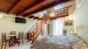 Un dormitorio con una cama, una escalera de madera, una mesa de comedor con sillas y un televisor en la pared.