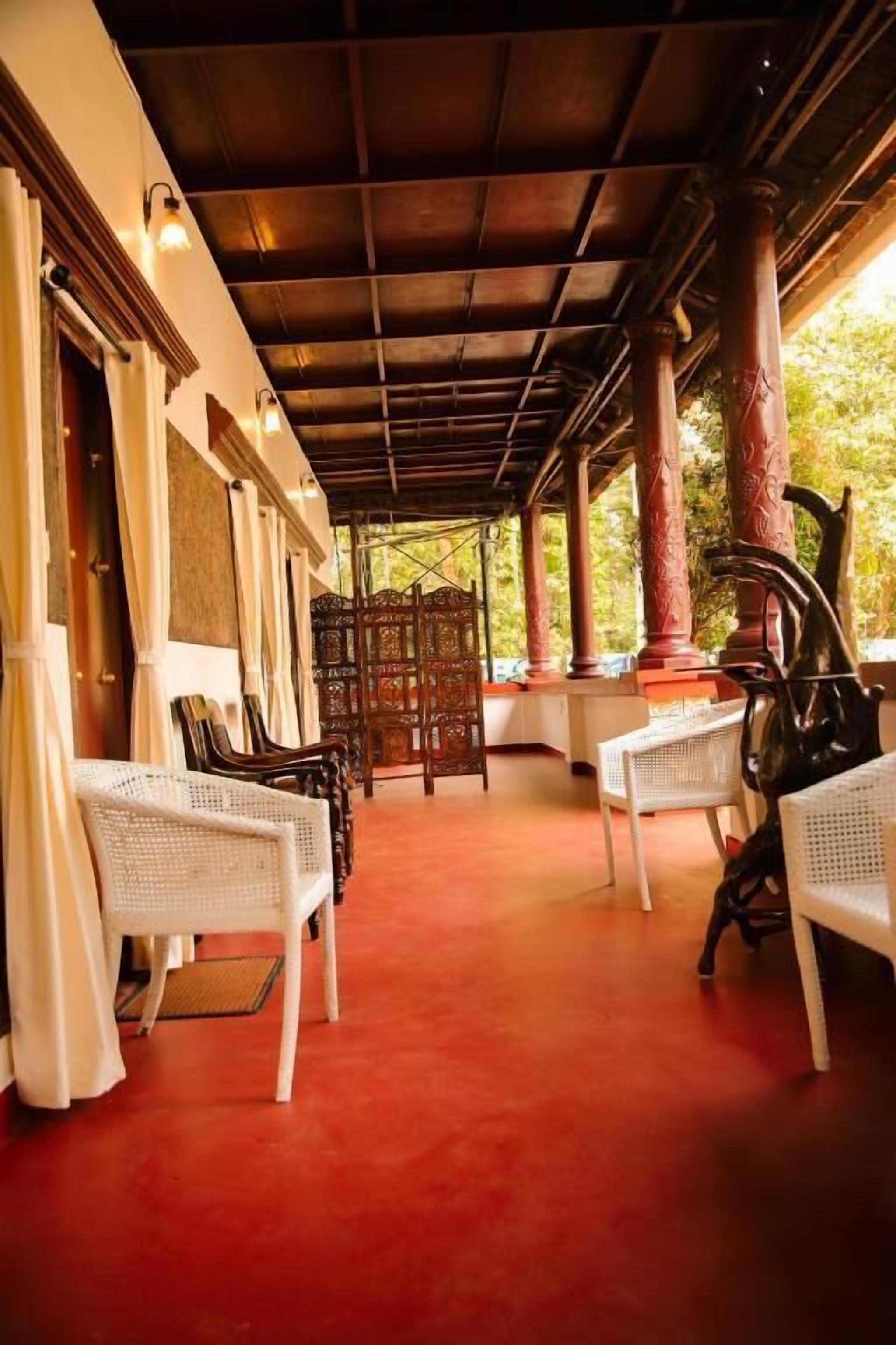 A covered outdoor seating area with white chairs and a table, surrounded by columns and a red carpet.