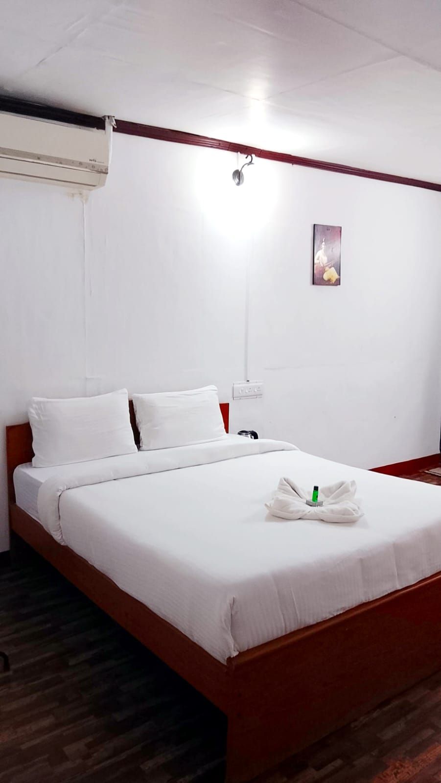 Een hotelkamer met een bed, wit beddengoed, een wandairconditioner, een nachtkastje en een wandlamp.