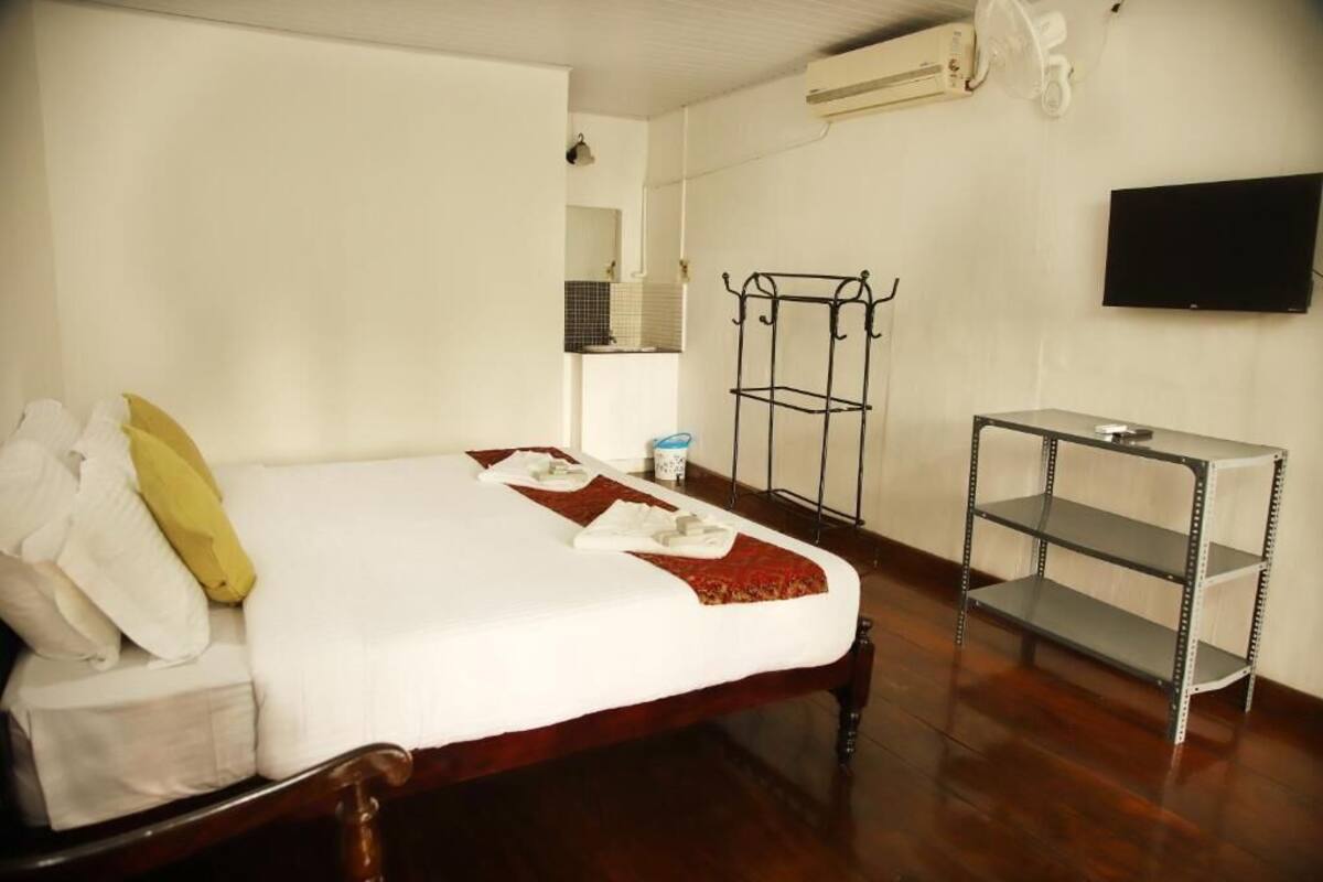 A hotel room with a wooden bed, a metal shelf, a television, and a small bathroom area.