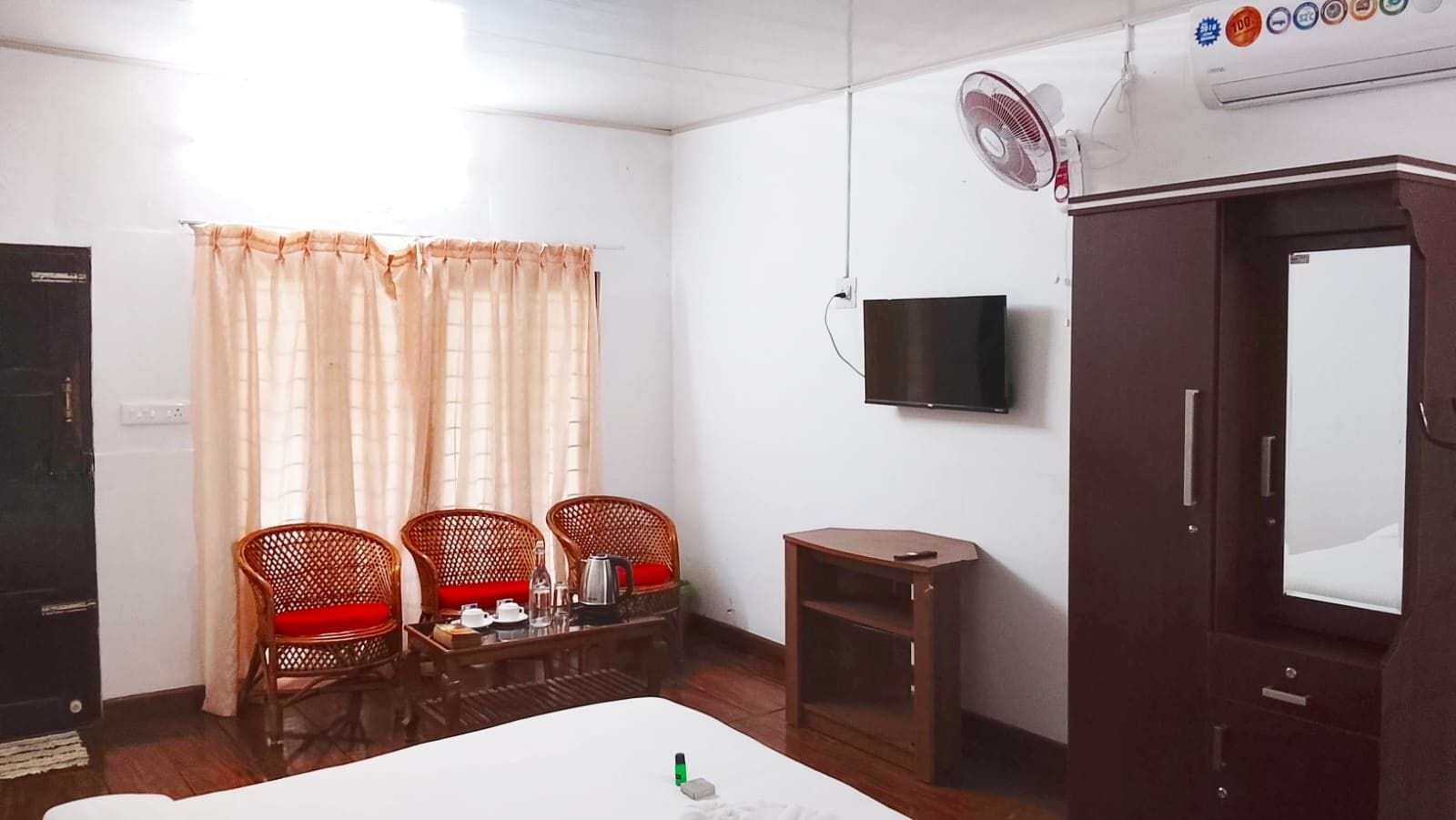 A room with a bed, a television mounted on the wall, a wooden cabinet, and a small table with chairs.