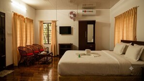 A hotel room with a bed, a TV, a fan, and a window with curtains. - Backwater Retreat Resort - Kumarakom (Kottayam)