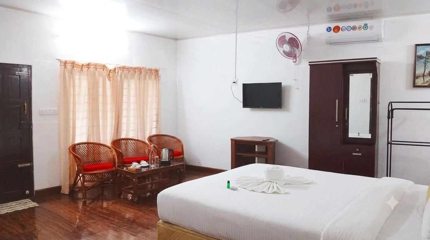 A hotel room with a bed, a desk with chairs, a TV, and a wardrobe.