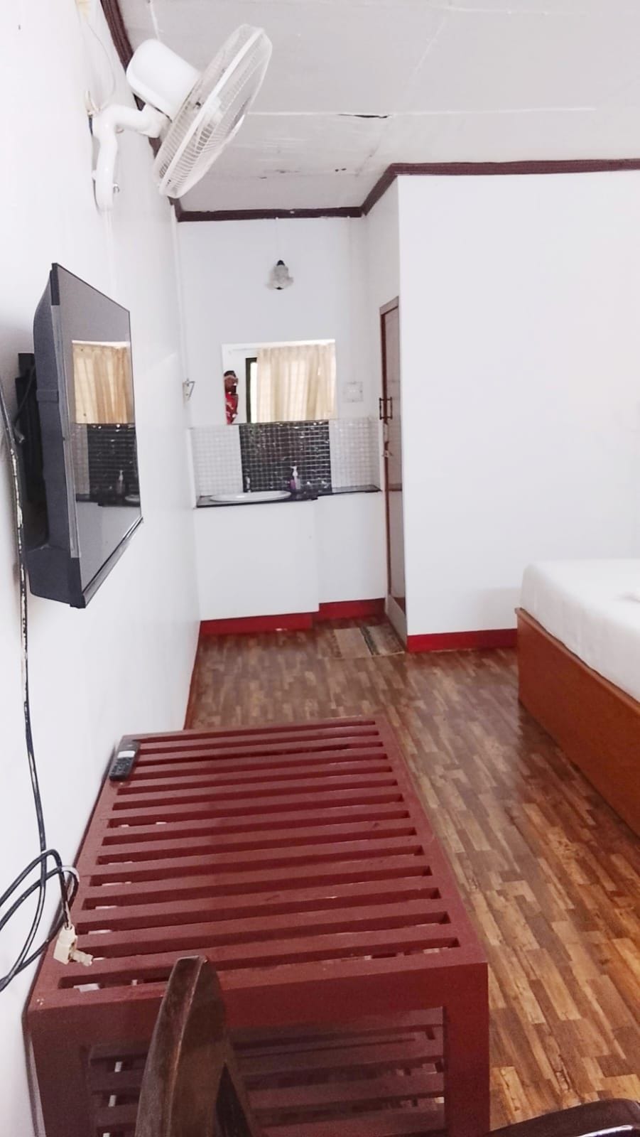 A room with a wooden floor, a bed, a TV mounted on the wall, and a window with curtains.
